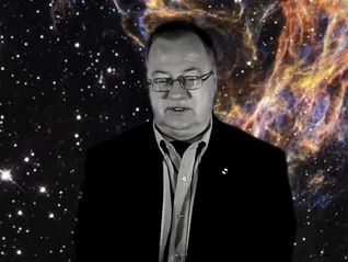 Black and white photo of a man wearing glasses and a suit against a star-filled black background with unearthly coloured filaments to the right