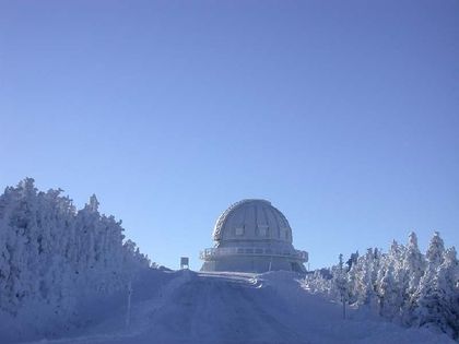 Photo of  a white dome located at the end of a wooded lane covered with a thick layer of white snow, with a blue sky as a backdrop