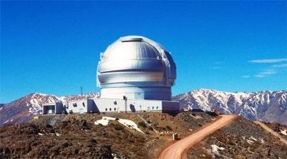 Photo of a silver-coloured observatory located on a hill with snow-covered mountains in the background
