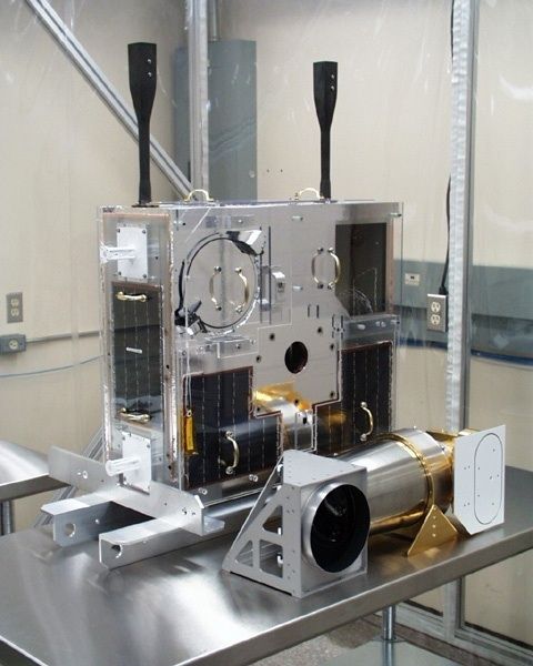 Colour photo of a rectangular telescope made of metal components positioned on a table in a closed room.