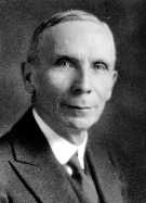 Photo en noir et blanc d'un homme de profil, regardant l'objectif et portant un complet avec une cravate