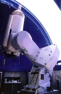 Photo of a telescope in front of a blue dome open to a very white sky