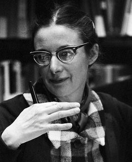 Black and white photo of a woman with glasses gesticulating in front of her shoulder with her right hand