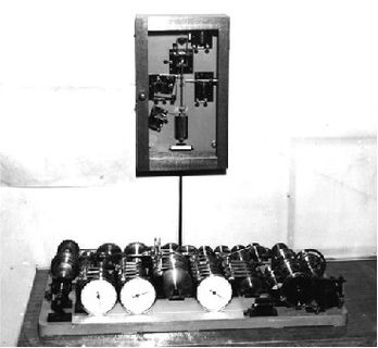 Photo en noir et blanc d'un mécanisme contenant une base remplie de tubes cylindriques, reliée à une boîte rectangulaire installée perpendiculairement au-dessus de la base.