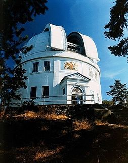 Colour photo of a white building with its dome open located at the top of a wooded hill