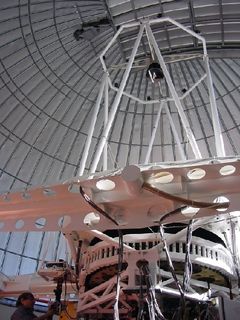 Photo en contre-plongée d'un télescope à la structure métallique blanche pointant vers le sommet d'un dôme fermé
