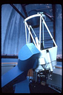 Photo de la structure bleue et blanche d'un télescope pointant vers le haut d'un dôme fermé