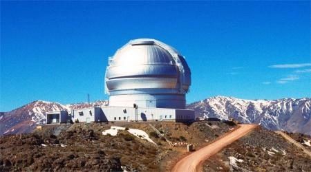 Photo of a silver-coloured observatory located on a hill with snow-covered mountains in the background