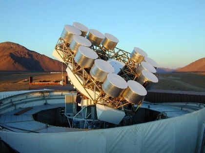 Photo de capteurs métalliques dorés pointant vers le ciel, installés sur le toit d'un l'observatoire, devant un paysage montagneux.