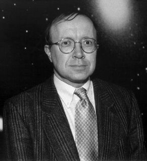 Black and white photo of a man with glasses wearing a suit with a star-filled sky in the background