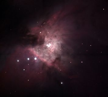 Photo of a nebula made up of very luminous white dots and pink-tinged clouds against a very black background