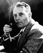 Photo en noir et blanc d'un homme assis de profil, regardant l'objectif en fumant la pipe