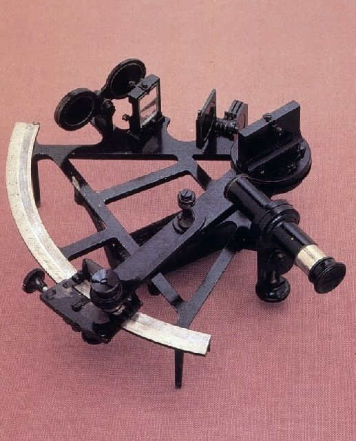 Photo couleur d'un sextant noir métallique constitué d'une règle graduée courbée d'un sixième de cercle, d'une lunette et d'une lentille