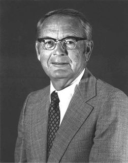 Black and white photo of a man wearing a suit and glasses with black rims.
