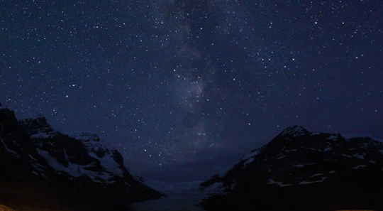Night photo of a midnight blue sky with thousands of stars above a mountainous landscape