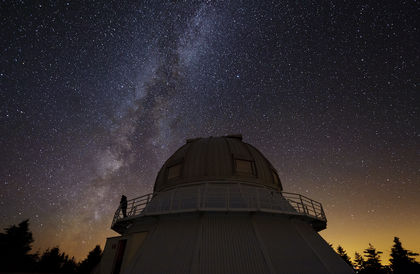 Night photo of a silhouette on the catwalk of an observatory under a star-filled sky at dusk